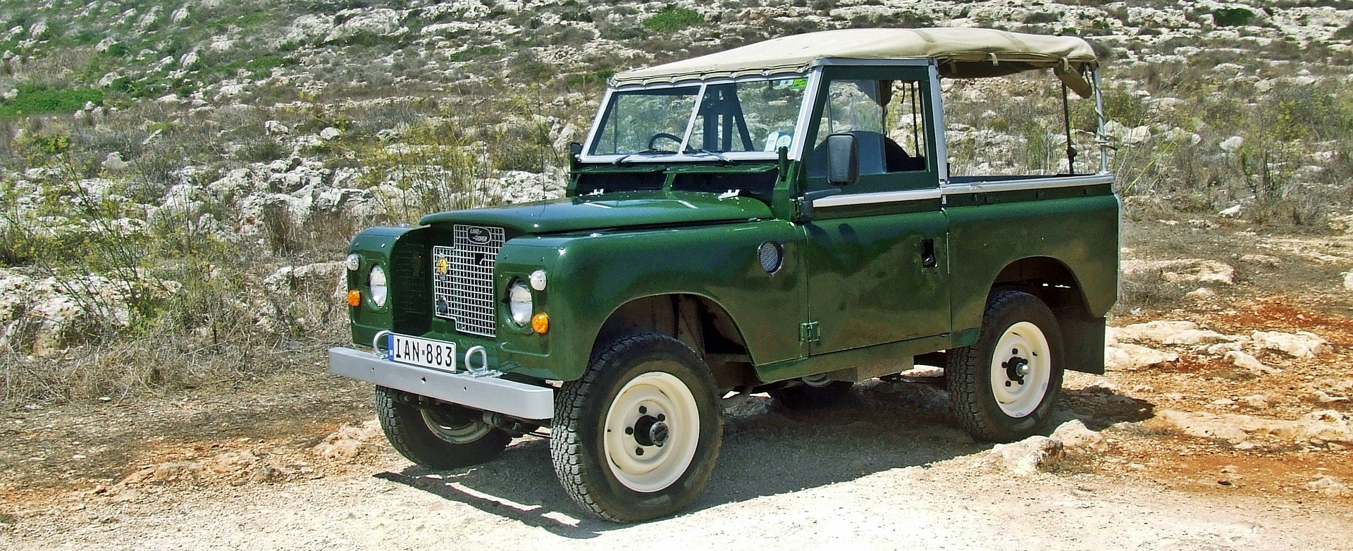 Un Land Rover vert foncé au milieu d'un paysage rocailleux et désertique